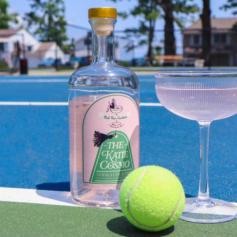 Katie Cosmo bottle with tennis ball and coupe glass on court